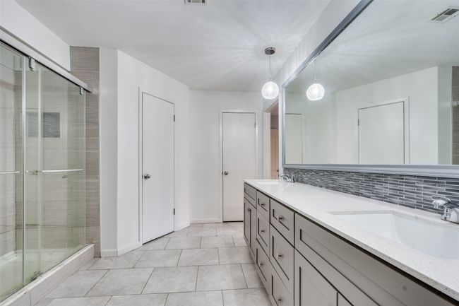 Bathroom featuring decorative backsplash, tile patterned floors, a shower with shower door, and vanity | Image 19