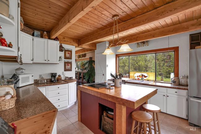 Kitchen with butcher block counters, a wooden ceiling with exposed beams, light tile patterned floors, and white cabinetry | Image 4