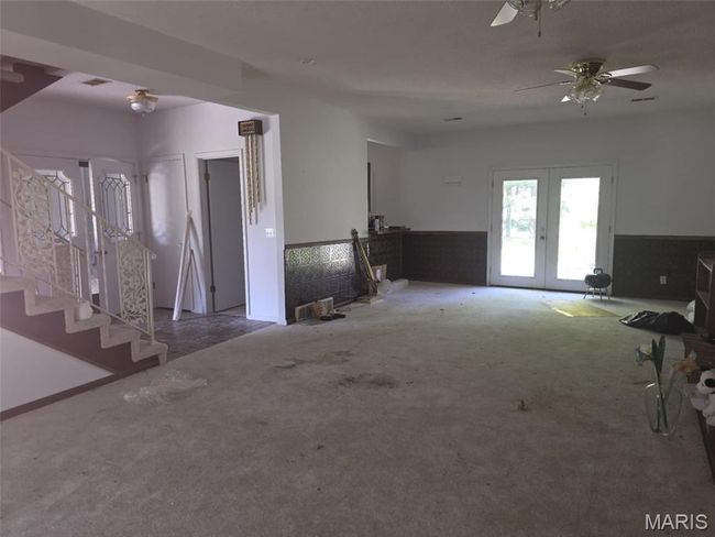 Unfurnished living room with carpet flooring, french doors, a wainscoted wall, ceiling fan, and stairs | Image 6