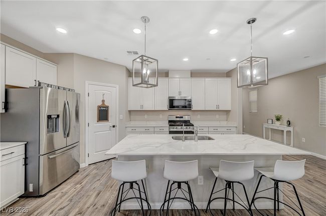 Kitchen featuring stainless steel appliances, light wood-style flooring, a sink, white cabinetry, and a breakfast bar | Image 25