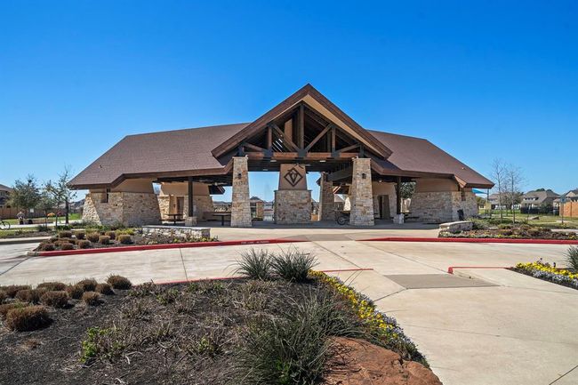 This photo features a spacious community pavilion with a rustic design, including stone pillars and a wooden roof. It's surrounded by landscaped grounds and pathways, ideal for gatherings and outdoor activities in a neighborhood setting. | Image 27