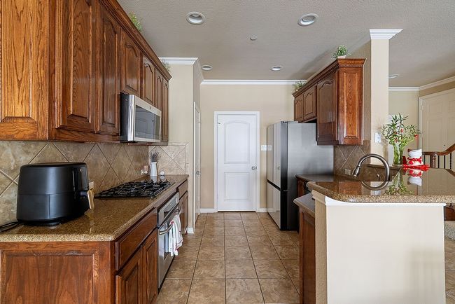 Kitchen with stainless steel appliances, tasteful backsplash, stone counters, a peninsula, and ornamental molding | Image 30