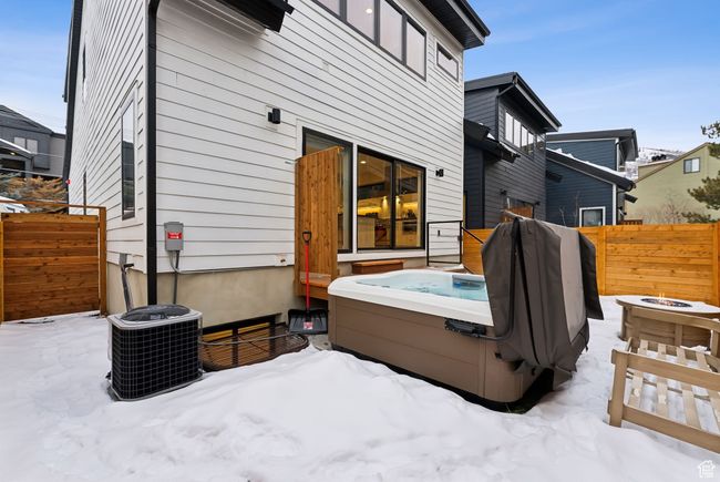 Snow covered back of property with an outdoor fire pit, cooling unit, and a hot tub | Image 14