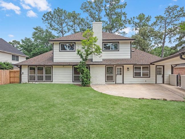 This photo showcases a charming two-story home with a spacious backyard and a large patio area. The exterior features a mix of siding and brick, with a central chimney. Surrounded by mature trees, it offers both privacy and a natural setting. | Image 35