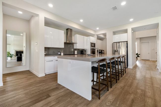 Kitchen featuring wall chimney range hood, stainless steel appliances, light wood-type flooring, a breakfast bar, and recessed lighting | Image 11