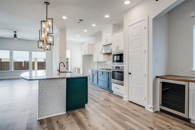 Kitchen with beverage cooler, ceiling fan, under cabinet range hood, stainless steel appliances, and light stone counters | Image 12