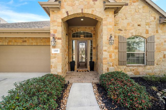 The covered entry features a stone archway, with decorative sconces adding a touch of elegance. A tandem garage completes the exterior. | Image 9