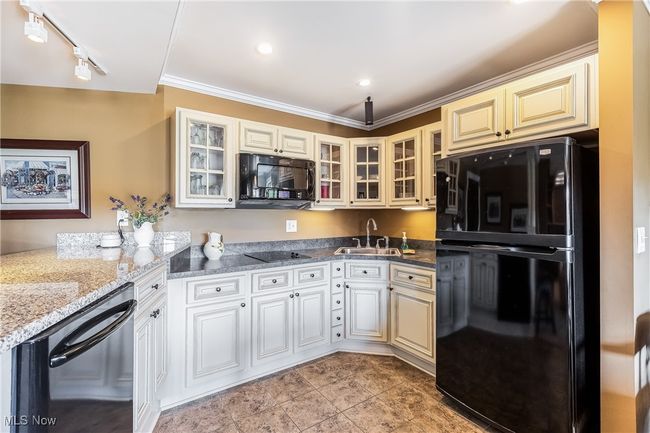 Kitchen featuring glass insert cabinets, a sink, light stone counters, and black appliances | Image 43
