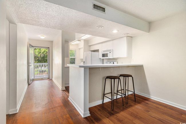 Kitchen with white appliances, a textured ceiling, dark wood-style flooring, a breakfast bar area, and a peninsula | Image 15