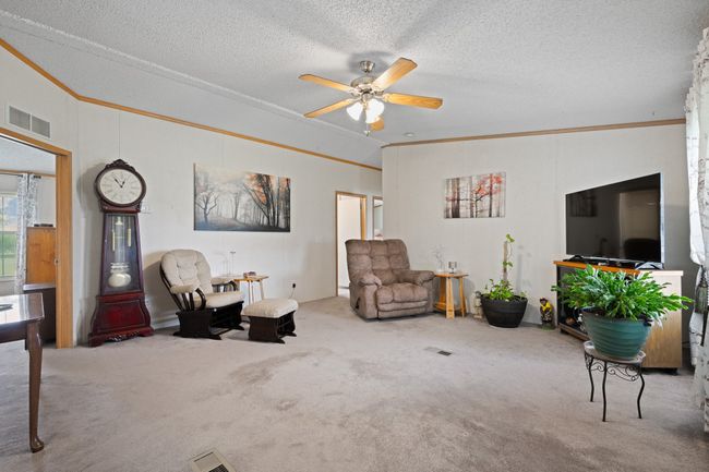 Living room with crown molding, a ceiling fan, carpet floors, and a textured ceiling | Image 6