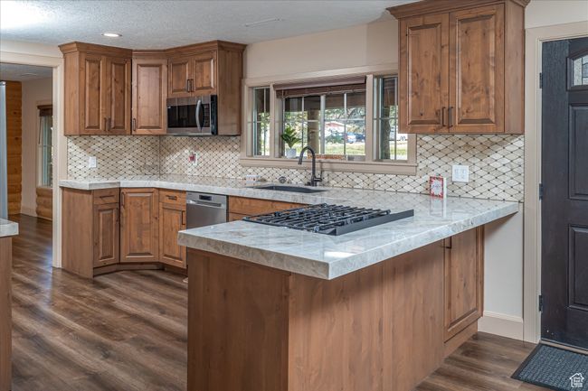 Kitchen featuring appliances with stainless steel finishes, a peninsula, dark wood-style flooring, brown cabinetry, and tasteful backsplash | Image 19