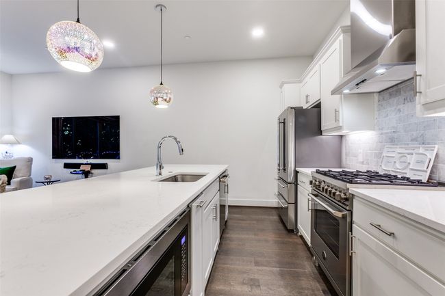 Kitchen featuring wall chimney range hood, backsplash, single basin sink, SS appliances and gorgeous quartz countertops! | Image 7