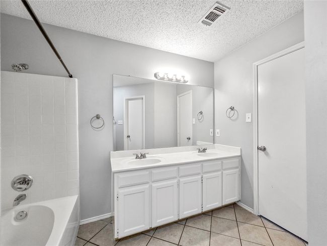 Full bath with tile patterned floors, a textured ceiling, double vanity, shower combination, and baseboards | Image 8