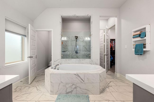 This primary bathroom is definitely move-in ready! Featuring a walk-in shower with tile surround, separate garden tub for soaking after a long day with custom tile detailing, dark stained cabinets with light countertops, spacious walk-in closet with shelving, high ceilings, neutral paint, sleek and modern finishes. | Image 11