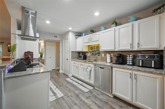 Kitchen featuring stainless steel dishwasher, island range hood, white cabinets, light wood-style floors, and recessed lighting | Image 11