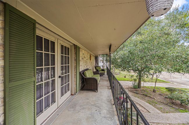 This photo shows French doors leading to a spacious front porch with green shutters, offering a cozy seating area perfect for relaxation. The balcony overlooks a well-maintained yard with mature trees, providing a pleasant and inviting outdoor space. | Image 26