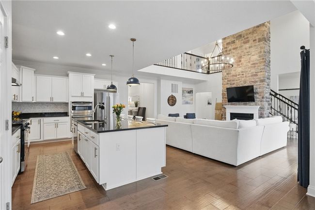Gourmet kitchen seamlessly connected to the great room, featuring white cabinetry, granite countertops, stainless steel appliances, and a spacious island with pendant lighting. Open-concept layout provides a perfect flow for entertaining and everyday living. | Image 12