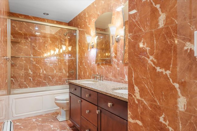 Bathroom featuring toilet, enclosed tub / shower combo, a sink, a baseboard heating unit, and tile walls | Image 14
