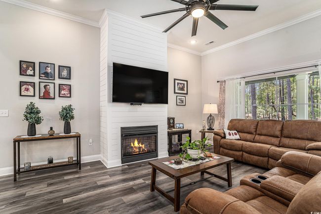 Living area with a ceiling fan, dark wood finished floors, baseboards, a fireplace, and crown molding | Image 15