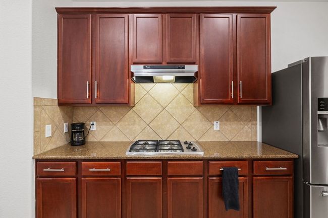 Kitchen featuring reddish brown cabinets, under cabinet range hood, stainless steel appliances, backsplash, and dark stone counters | Image 14