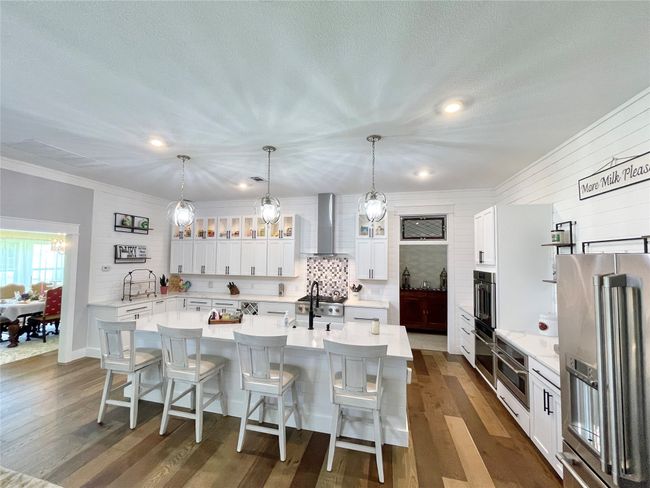 Kitchen with wall chimney exhaust hood, stainless steel fridge, a kitchen island with sink, light countertops, and recessed lighting | Image 12