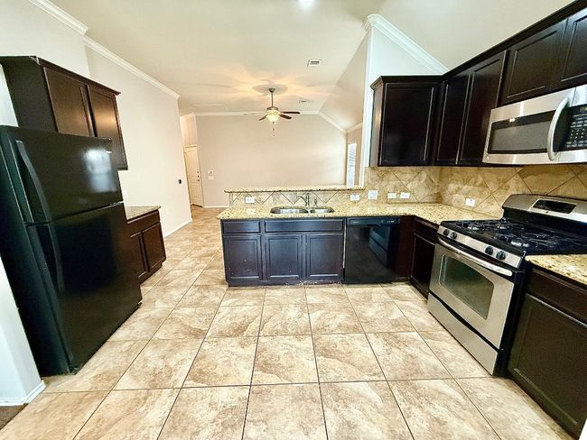 Kitchen with black appliances, ceiling fan, tasteful backsplash, crown molding, and a peninsula | Image 4