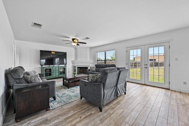 Living room with wood finished floors, french doors, a ceiling fan, a fireplace, and baseboards | Image 7