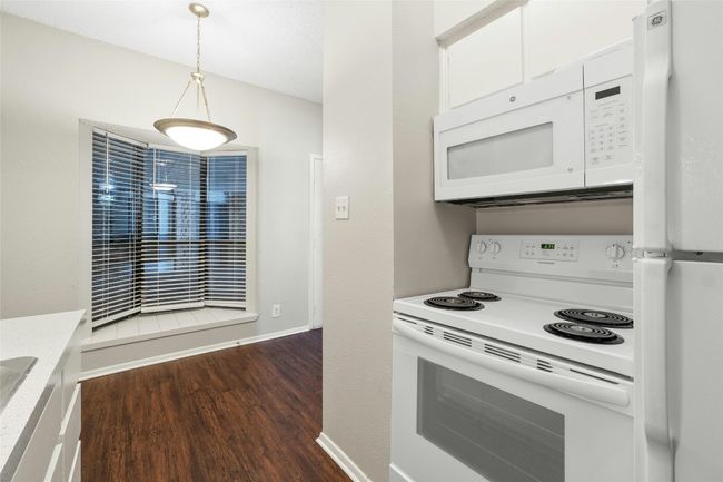 Kitchen with white appliances, white cabinetry, light countertops, hanging light fixtures, and dark wood finished floors | Image 12