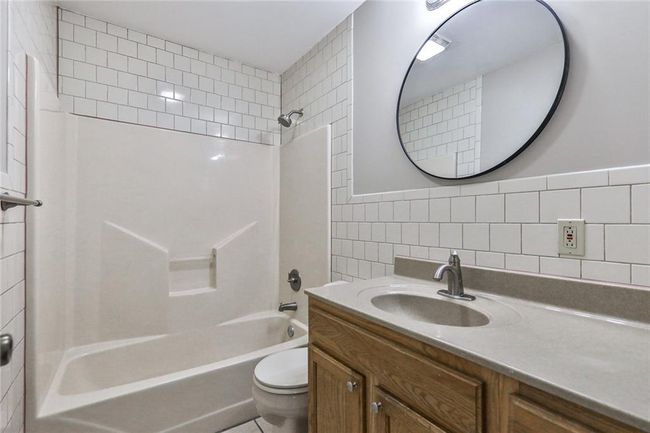 Full bathroom featuring shower / bathing tub combination, vanity, toilet, and tile walls | Image 11