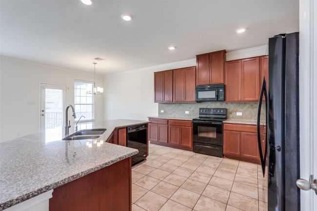 Kitchen featuring light tile patterned floors, ornamental molding, black appliances, a sink, and backsplash | Image 10