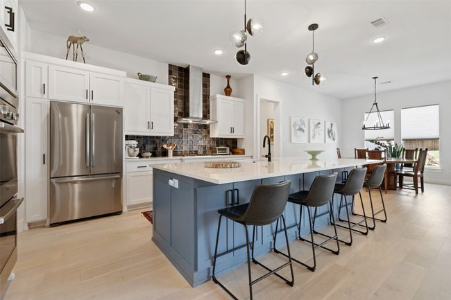 Kitchen with stainless steel appliances, a large island, white cabinets, wall chimney exhaust hood, and tasteful backsplash | Image 9