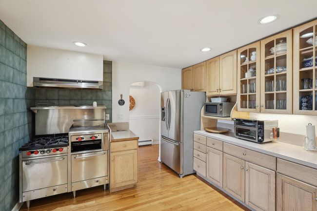 Kitchen featuring arched walkways, light wood-type flooring, appliances with stainless steel finishes, baseboard heating, and under cabinet range hood | Image 15