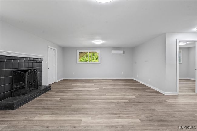 Unfurnished living room featuring a wall mounted air conditioner, a tile fireplace, wood finished floors, and baseboards | Image 25