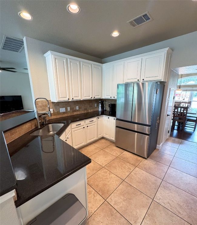 Kitchen with freestanding refrigerator, backsplash, white cabinetry, recessed lighting, and light tile patterned floors. | Image 9