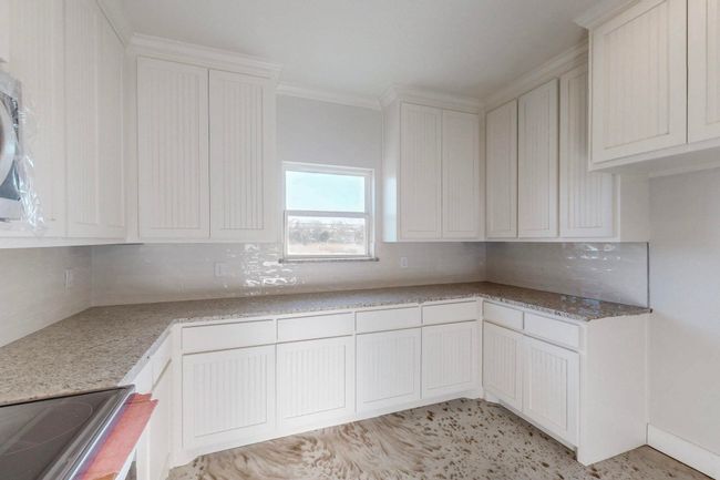Kitchen with tasteful backsplash, white cabinetry, and crown molding | Image 16