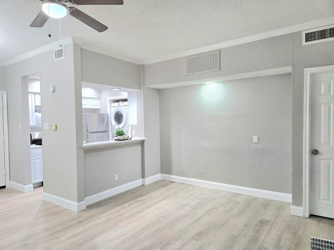 Unfurnished room with crown molding, light wood-type flooring, stacked washer and clothes dryer, ceiling fan, and baseboards | Image 6