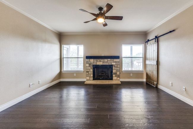 Unfurnished living room featuring a barn door, hardwood / wood-style floors, a ceiling fan, ornamental molding, and a fireplace | Image 5