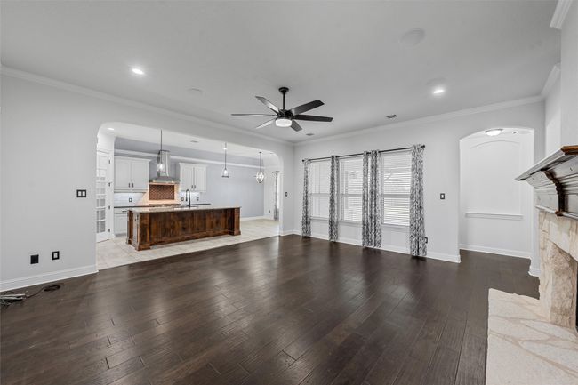 Unfurnished living room with arched walkways, a ceiling fan, light wood finished floors, a fireplace, and ornamental molding | Image 5