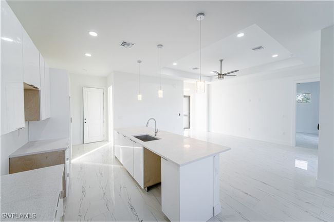 Kitchen featuring white cabinetry, sink, a tray ceiling, and an island with sink | Image 8