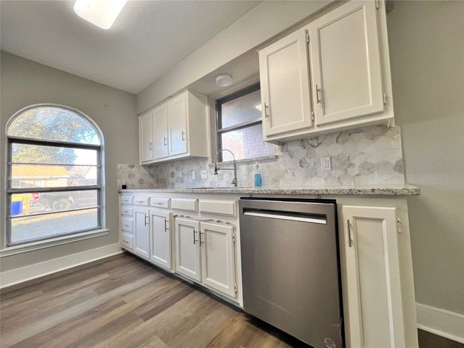 Kitchen with light wood-type flooring, stainless steel dishwasher, white cabinets, and light stone counters | Image 9