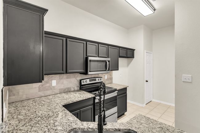 Kitchen with stainless steel appliances, decorative backsplash, light stone countertops, and light tile patterned floors | Image 9