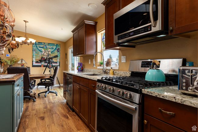 Kitchen with appliances with stainless steel finishes, pendant lighting, sink, light stone counters, and light wood-type flooring | Image 10