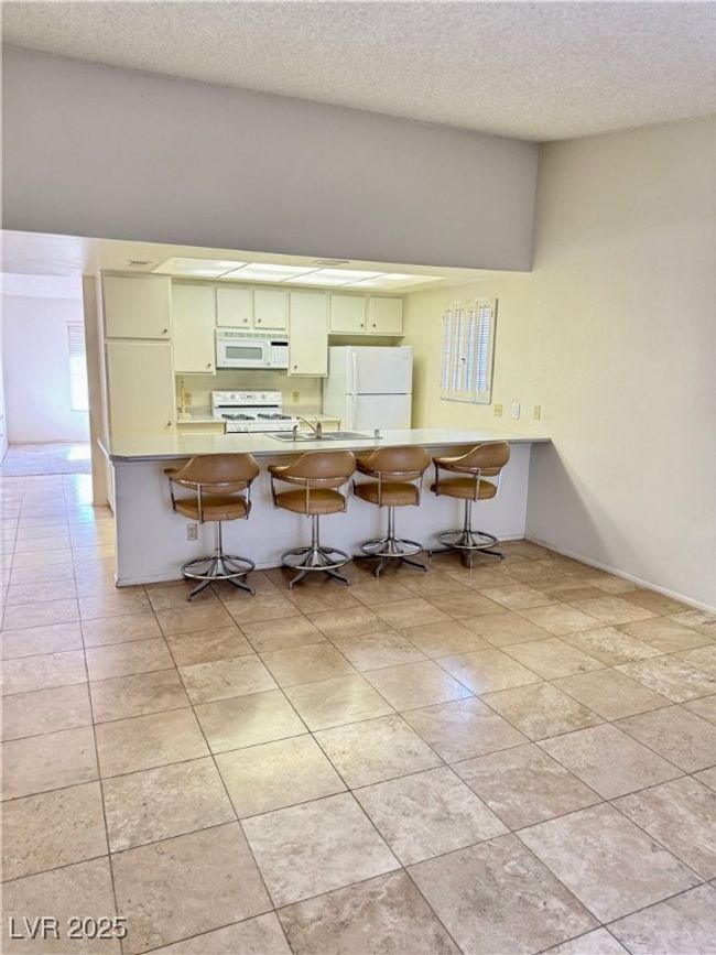 Kitchen featuring white appliances, a kitchen breakfast bar, light tile patterned floors, a textured ceiling, and a peninsula | Image 17