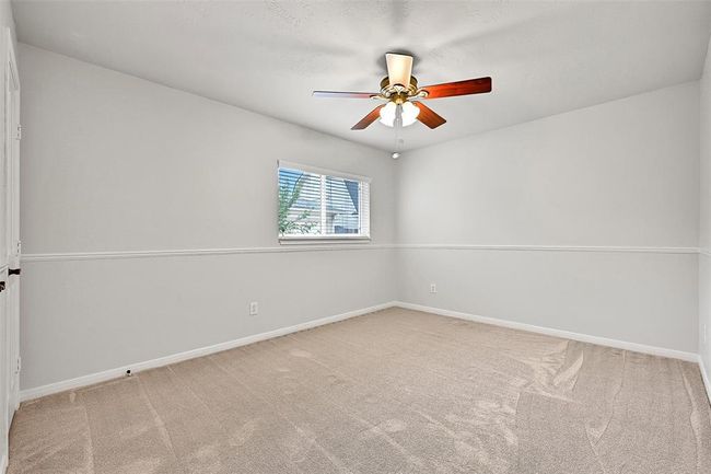 The first of two secondary bedrooms features soft neutral carpet, light grey paint with a crisp white chair rail accent, a lighted ceiling fan, and a spacious double-door closet. | Image 19