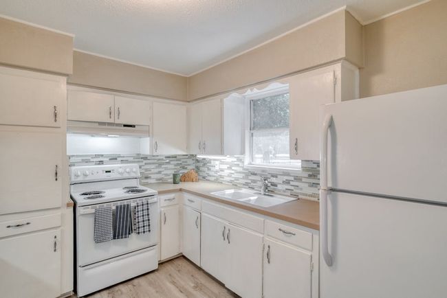 Kitchen with light countertops, white cabinets, a sink, white appliances, and under cabinet range hood | Image 13