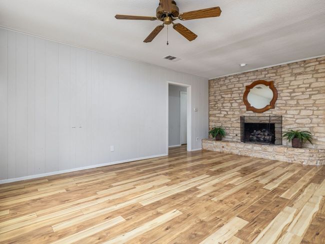 Unfurnished living room featuring wood-type flooring, a large fireplace, ceiling fan, and crown molding | Image 5