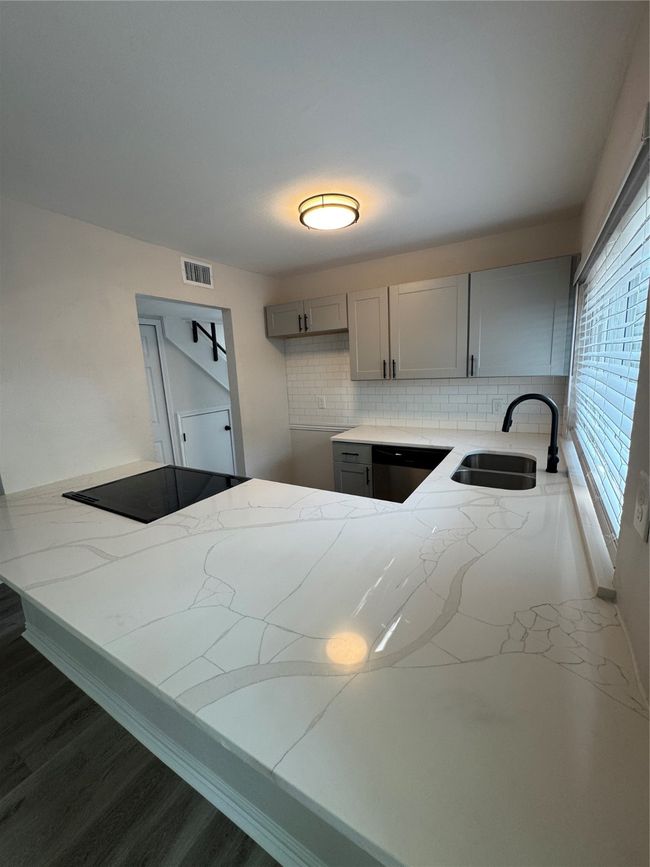 Kitchen featuring a sink, light stone countertops, gray cabinetry, tasteful backsplash, and dishwashing machine | Image 5
