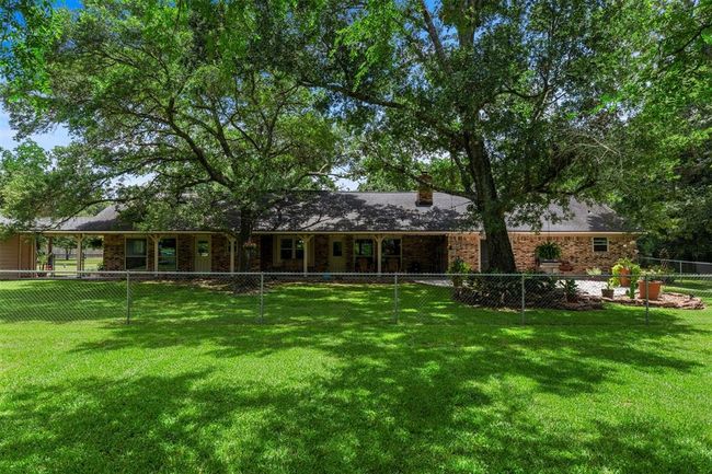 This photo shows a charming brick home with a spacious, fenced yard. Large trees provide shade, and the property features a well-maintained lawn and a cozy patio area, ideal for outdoor relaxation. | Image 22