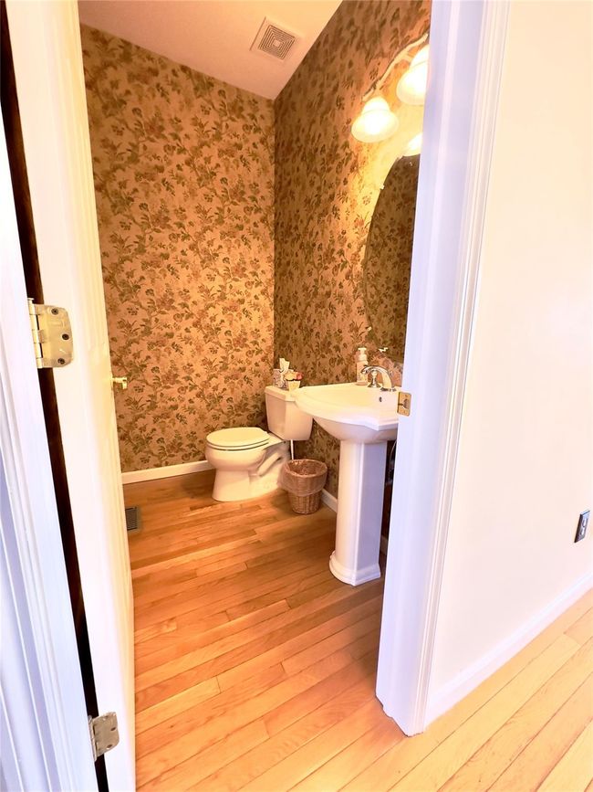 First Floor Half Bathroom featuring wood-type flooring, visible vents, toilet, baseboards, and wallpapered walls | Image 5
