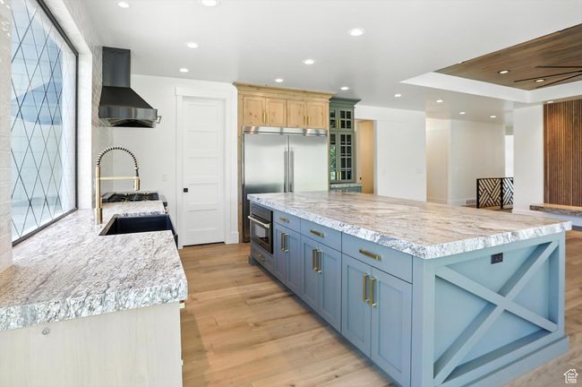 Kitchen featuring wall chimney exhaust hood, light wood-style flooring, recessed lighting, glass insert cabinets, and a kitchen island | Image 13
